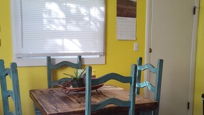 A dining area with a wooden table and turquoise chairs, yellow walls, a calendar, and a window with blinds.