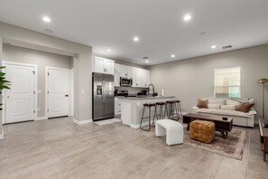 A modern kitchen with white cabinets, a stainless steel refrigerator, and a microwave. There is a dining area with a sofa and a coffee table. - Experience comfort in the Stunning Lawrence, a spacious 2-bedroom, 2-bathroom retreat (Phoenix)