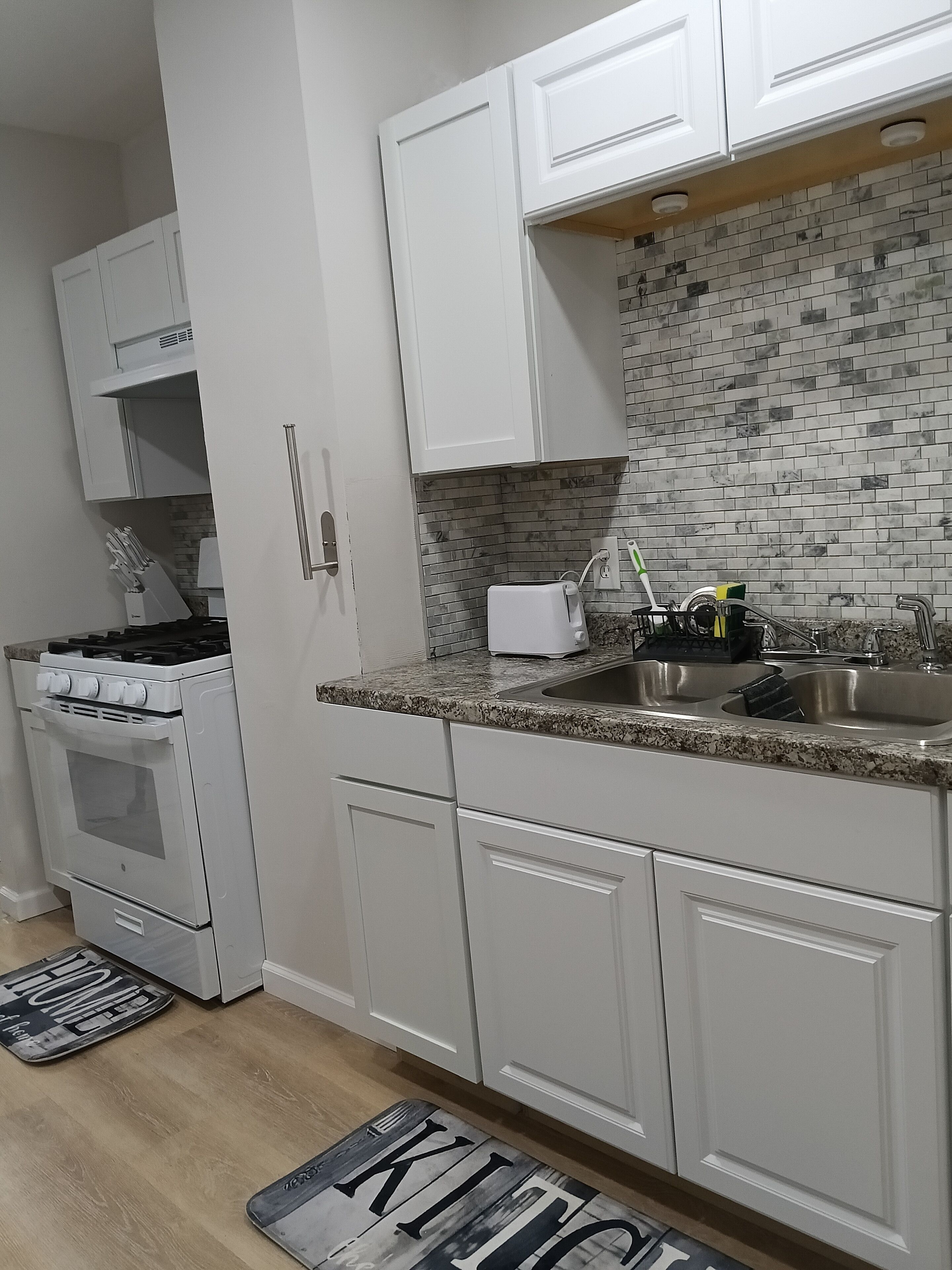A modern kitchen with white cabinetry, a tiled backsplash, a gas stove, and a stainless steel sink.