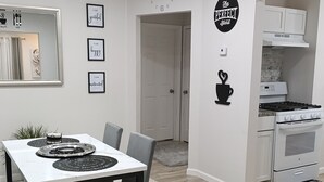 Une cuisine moderne avec des meubles blancs, un four encastré et un coin repas comprenant une table blanche et des chaises noires.