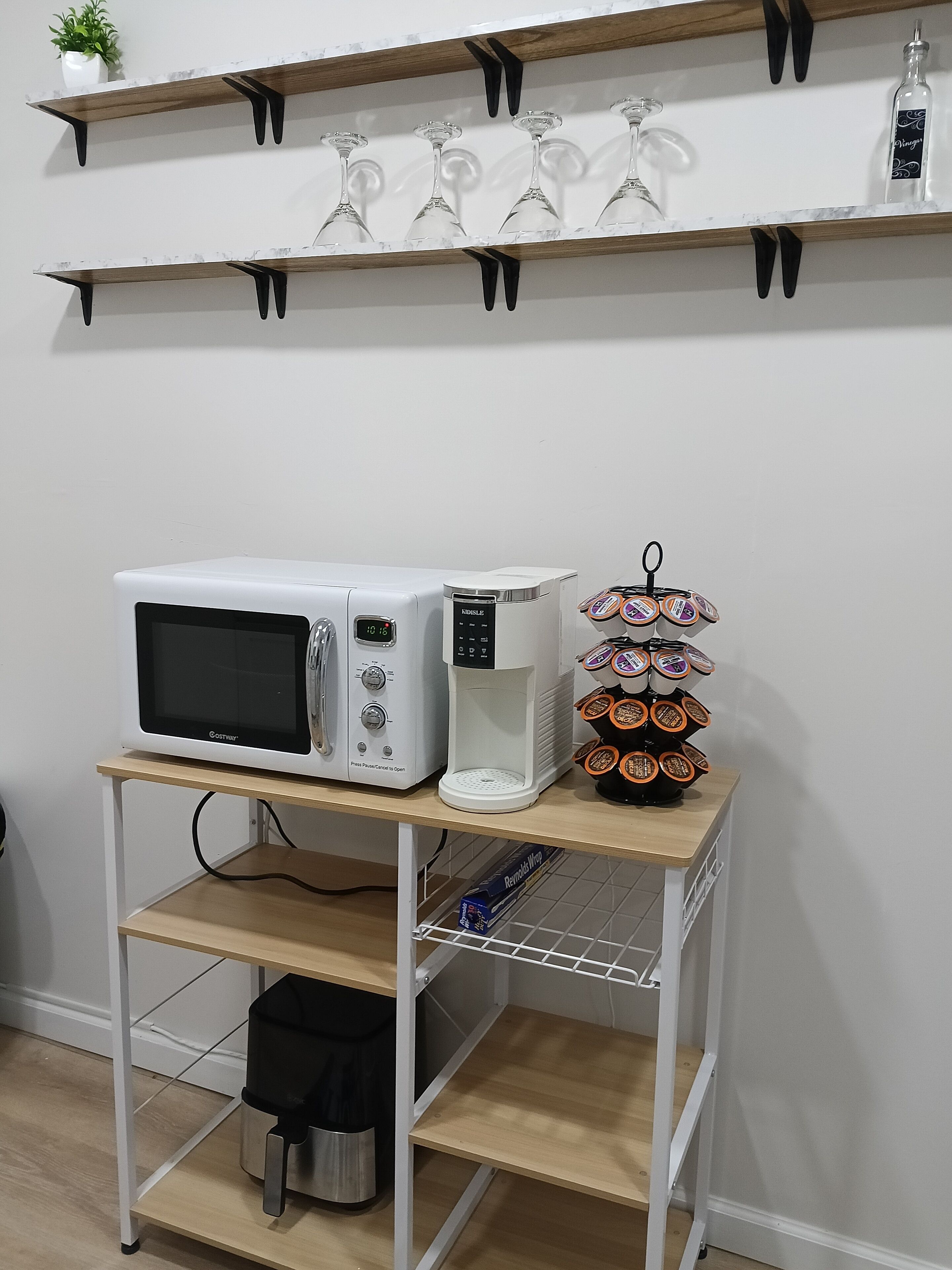 A kitchen area with a microwave, coffee maker, and a coffee pod holder on a cart.