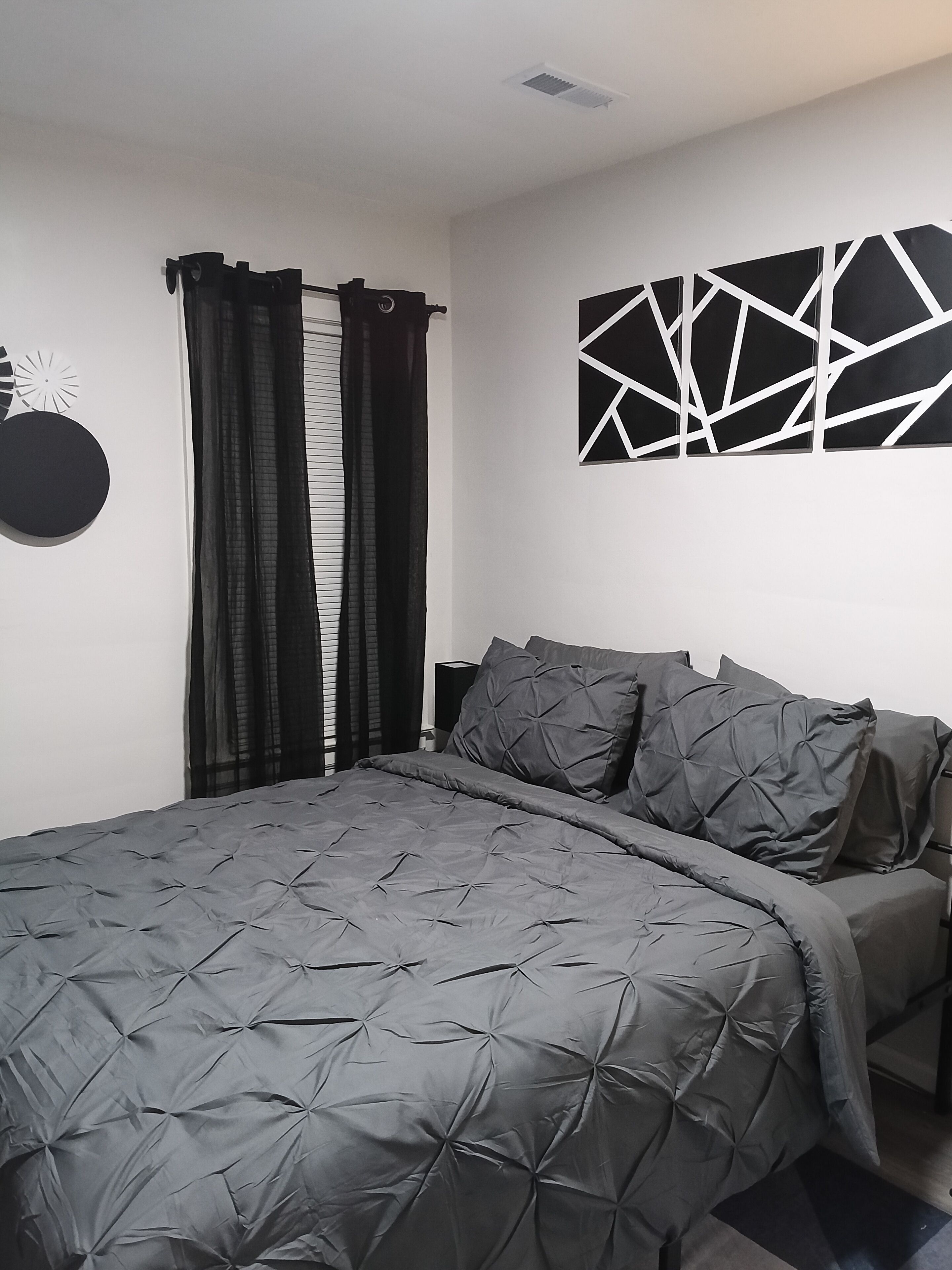 A bedroom with a bed, dark curtains, a wall-mounted abstract art piece, and a circular decoration.