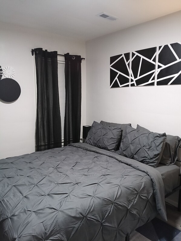 A bedroom with a bed, dark curtains, a wall-mounted abstract art piece, and a circular decoration.