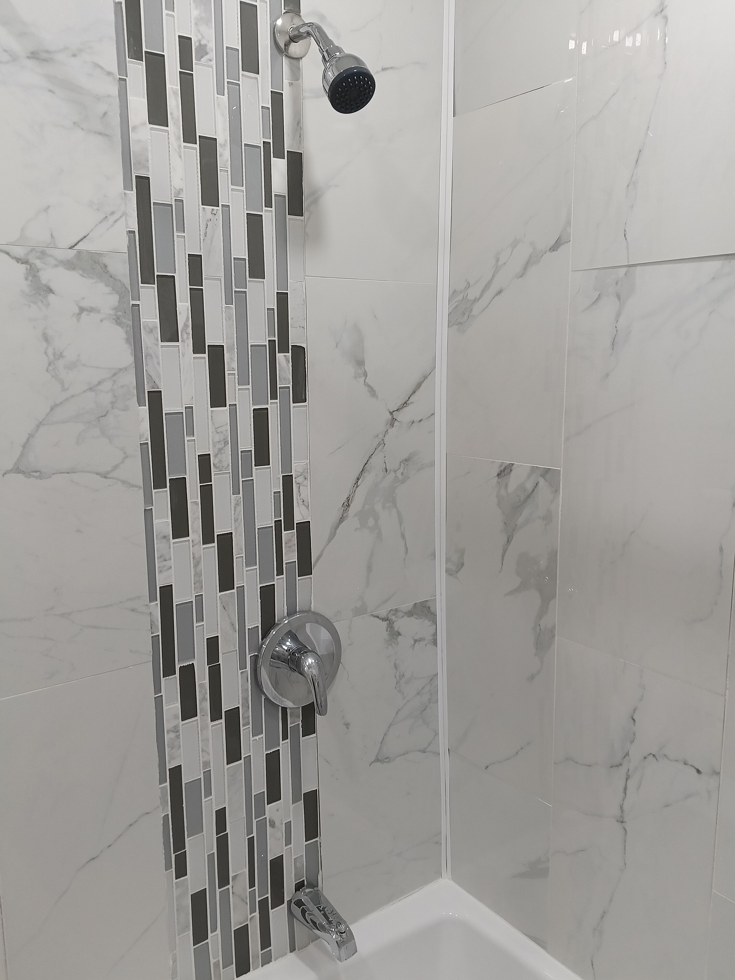 A shower with a modern design, featuring a vertical mosaic tile pattern and a handheld showerhead.