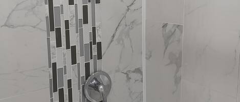 A shower with a modern design, featuring a vertical mosaic tile pattern and a handheld showerhead.