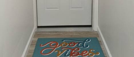 Een witte deur met een zilveren handvat en een deurmat met de tekst 'Good Vibes, All the Time'.