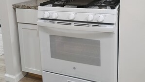 Une cuisine avec un four, une cuisinière et un four à micro-ondes, tous de couleur blanche. On y trouve un bloc à couteaux sur le comptoir et un pare-feu décoré d'un motif en briques.