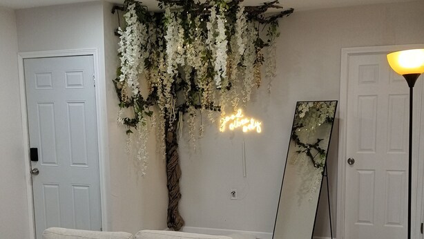 Un salon avec un canapé blanc, une plante suspendue, un néon et une lampe sur pied.