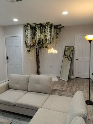 A living room with a white sofa, a hanging plant, a neon sign, and a floor lamp.
