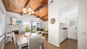 Una cocina moderna con armarios blancos, un comedor con mesa y sillas de madera, y un ventilador de techo.