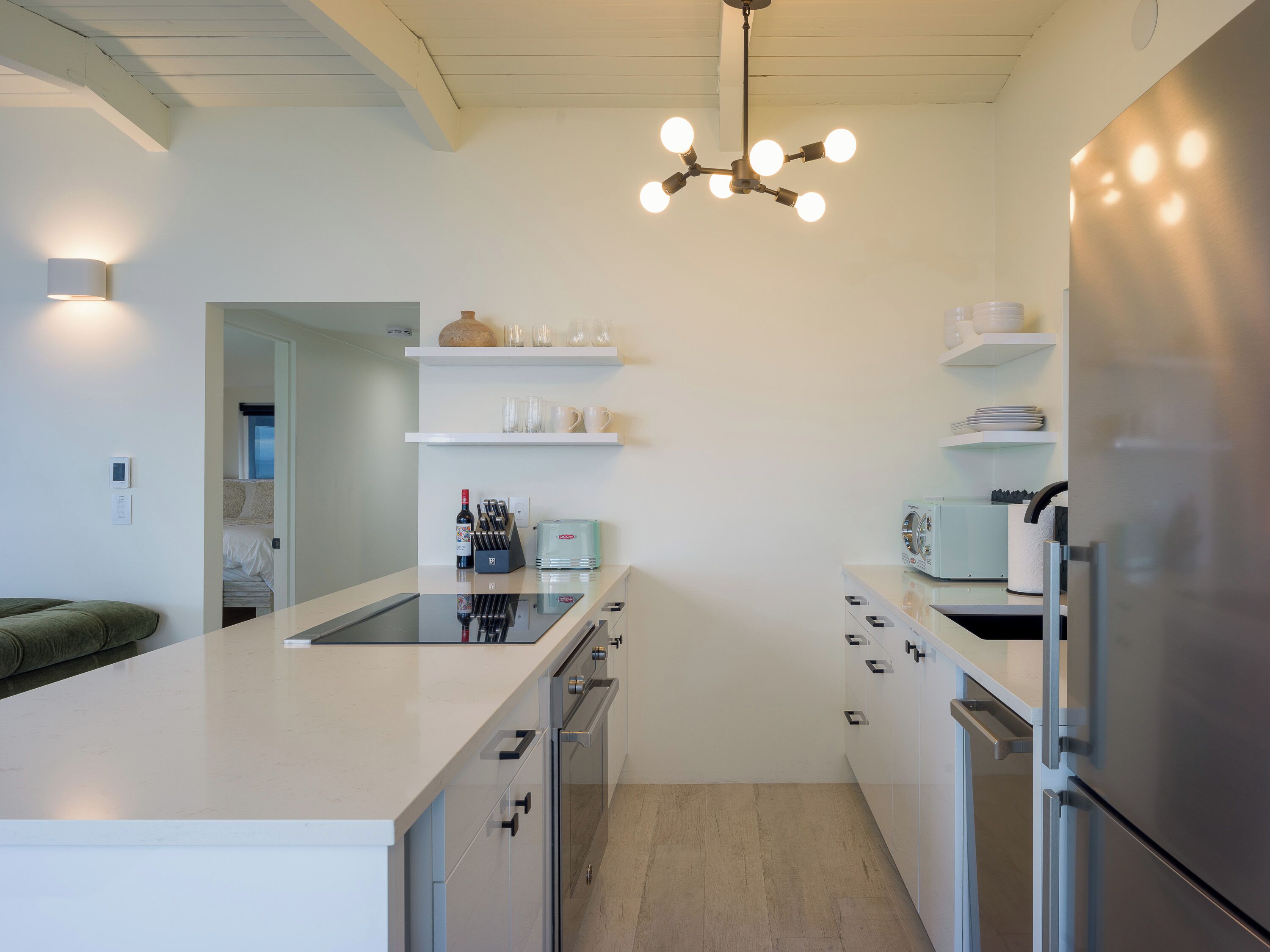 Une cuisine moderne dotée d’un grand îlot central, d’appareils électroménagers en acier inoxydable et d’un luminaire suspendu.