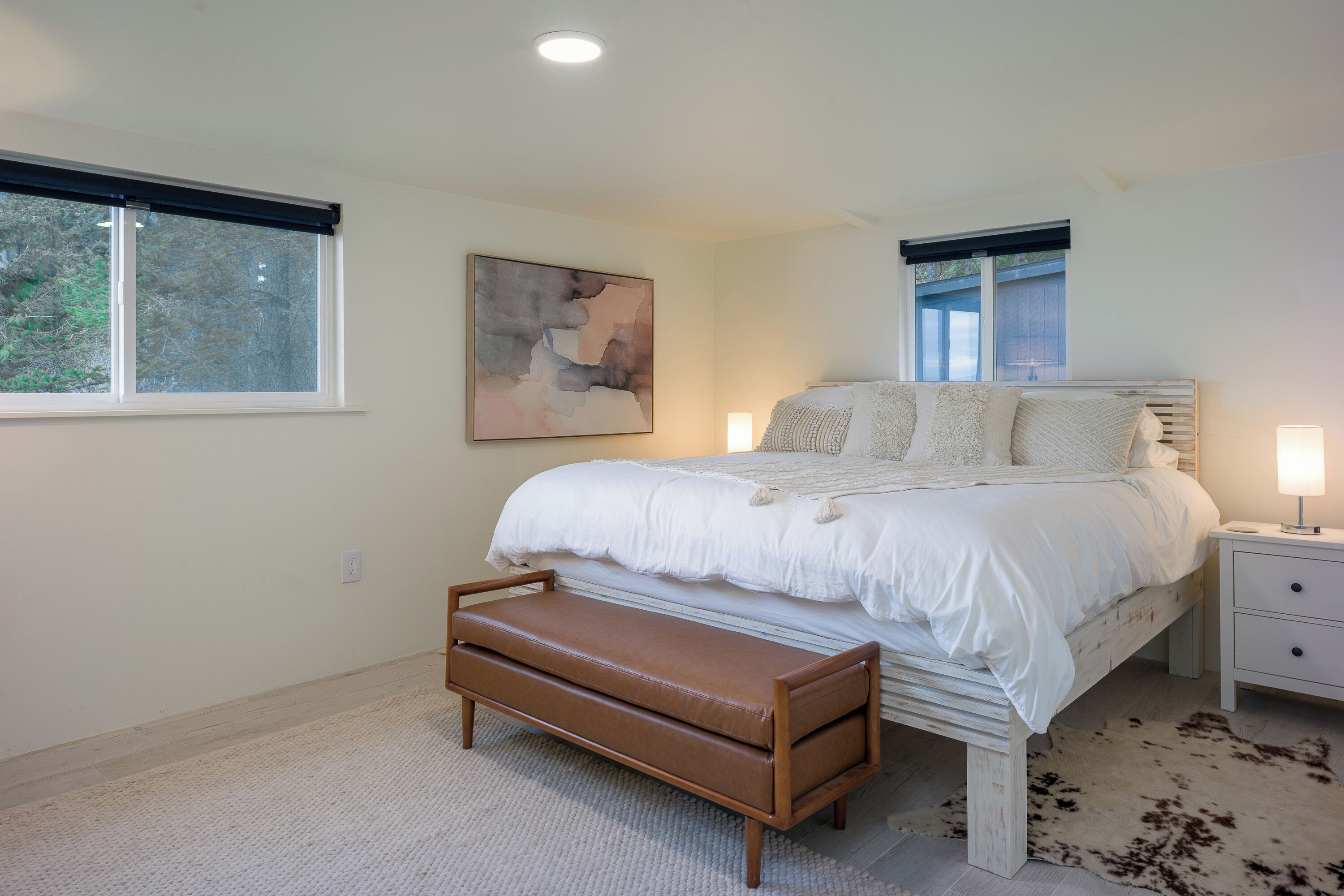 Een slaapkamer met een bed, een bankje, nachtkastjes en een schilderij aan de muur.