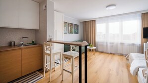 A modern, well-lit room with a kitchen area, a dining table, and a bed. - Wola Smocza Pleasant Studio (Warszawa)