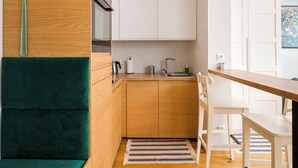 A compact kitchen with wooden cabinets, a stainless steel sink, and a green chair. - Wola Smocza Pleasant Studio (Warszawa)