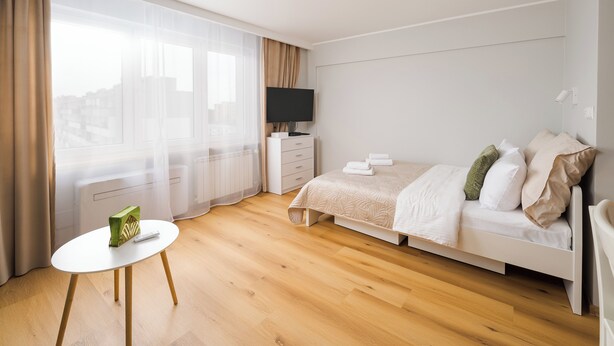 A modern hotel room with a bed, a TV, a small table, and a window with curtains. - Wola Smocza Pleasant Studio (Warszawa)