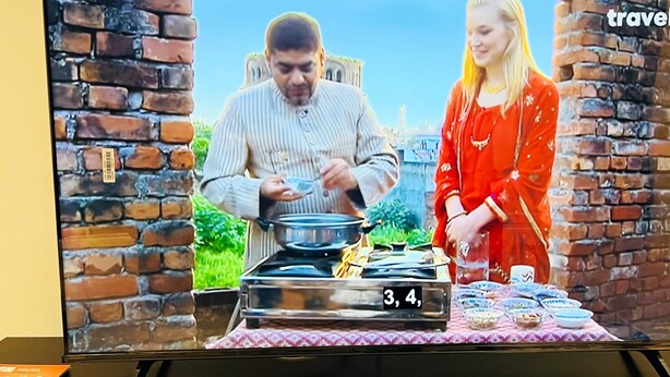 A television screen displaying a cooking scene with a brick wall and a clear sky in the background. - Ground Floor Entire Holiday Apartment - Self Check in/out - Perfect for 6 Guests (Crossgates)