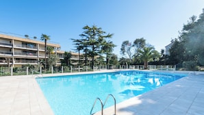 Une piscine dotée d’une terrasse carrelée, entourée d’une clôture et de palmiers.