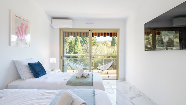 Une chambre d’hôtel avec deux lits, un balcon avec des chaises et une vue sur les arbres.