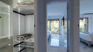 Une chambre d’hôtel comprenant un lit, un coin salon avec un fauteuil, un balcon avec une table, ainsi qu’une salle de bain avec une douche et des toilettes.
