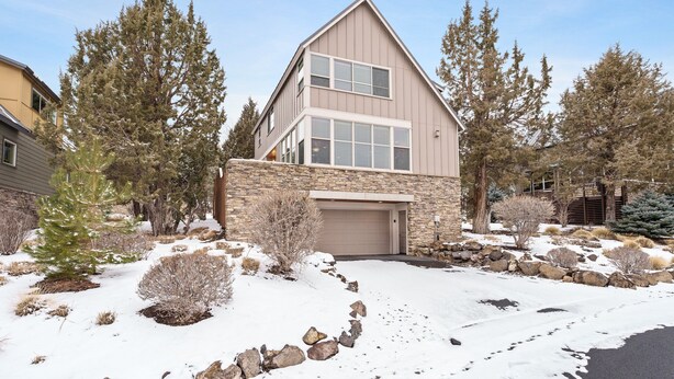 Une maison à deux étages avec une façade en pierre, un garage et une allée recouverte de neige.