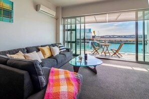 Relax in this stylish living room with a sofa, coffee table, and dining area offering a view of a body of water and the city.