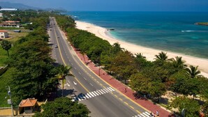 A coastal road with a beach on one side, lined with trees and buildings. - 3-bedroom apartment in marvelous Puerto Plata with AC, WiFi (Puerto Plata)