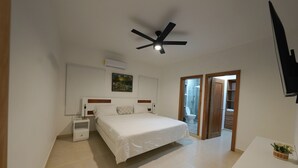 A bedroom with a bed, bedside tables, a ceiling fan, a TV, and a bathroom visible through an open door. - 3-bedroom apartment in marvelous Puerto Plata with AC, WiFi (Puerto Plata)