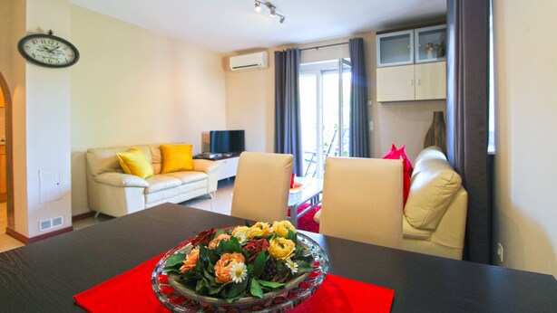 Una sala de estar con un sofá, una mesa de comedor con un centro de mesa floral, un televisor y un reloj en la pared.