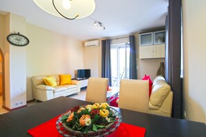 Ett vardagsrum med en soffa, ett matbord med en blomsterdekoration i mitten, en tv och en klocka på väggen.