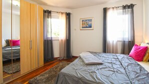 Un dormitorio con cama, armario, cuadro y ventana con cortinas.