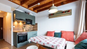 A compact kitchen with modern appliances, a dining area with a table and stools, and a cozy seating area with cushions. - Cosy mezzanine studio for 4 ppl (Morillon)