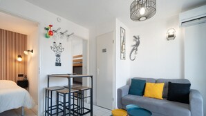 Een moderne, goed verlichte kamer met een grijze bank, een eettafel en een bed.