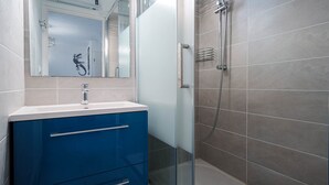 Een moderne badkamer met een glazen douchecabine, een witte wastafel met een blauwe kast, en een spiegel met decoratieve lijst.