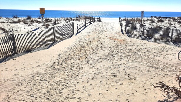 A sandy beach path with wooden fences and signs, leading to the ocean.