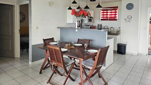 Un coin repas avec une table et des chaises en bois, une cuisine à l’arrière-plan et un ventilateur de plafond.
