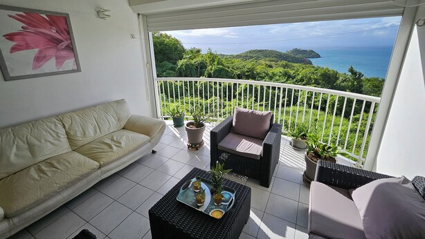 Un balcon avec un canapé, deux fauteuils, une table basse et des plantes en pot.