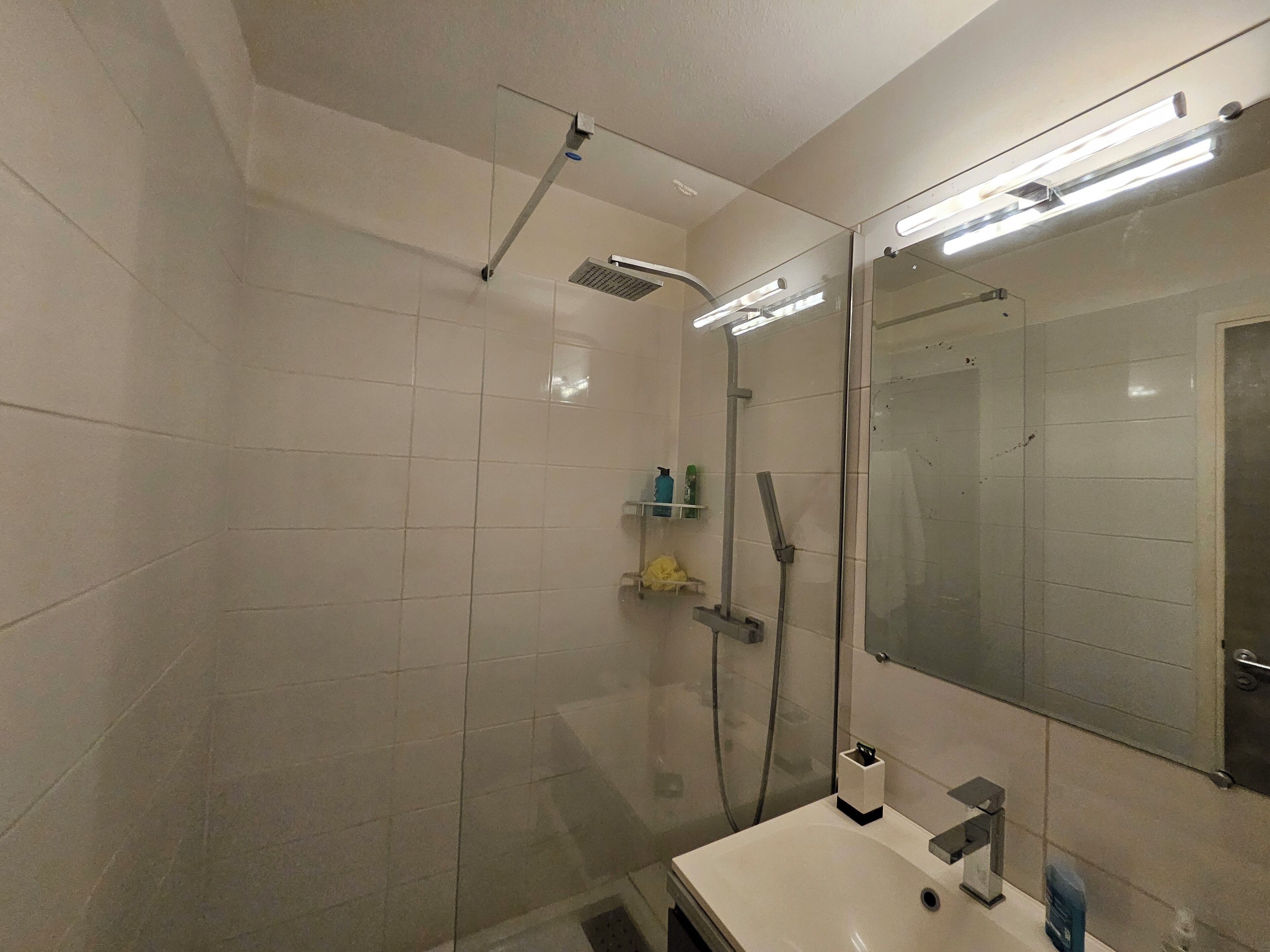 Une salle de bain moderne avec une douche à parois de verre, un grand miroir et un lavabo blanc.
