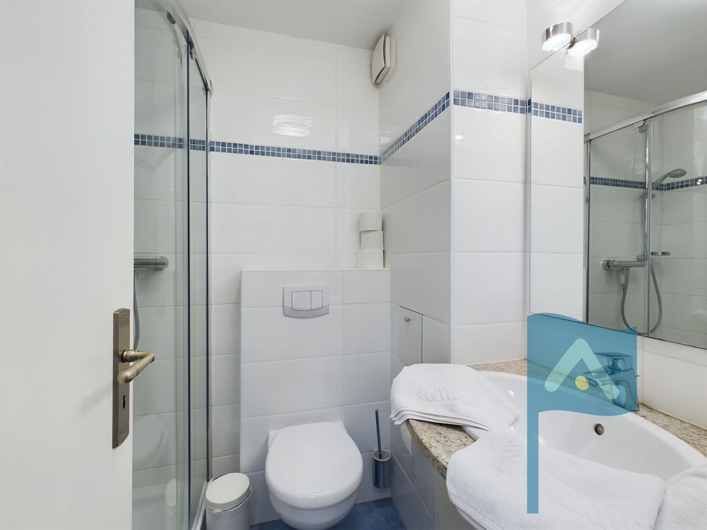 Un baño moderno con cabina de ducha de vidrio, inodoro y lavamanos con una toalla.