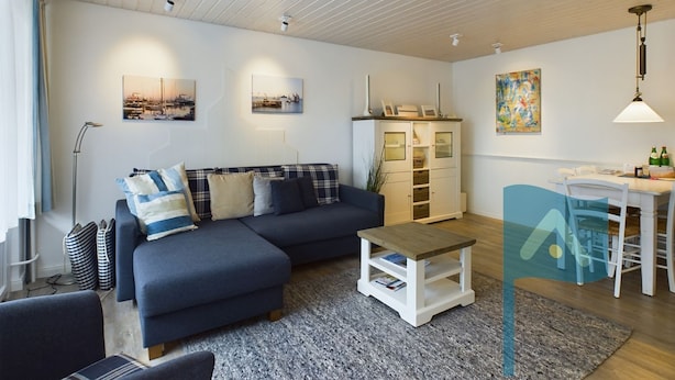 A modern living room with a dark blue sofa, a white cabinet, and a dining area with a table and chairs. - In 2nd row to the beach - Gmelinstraße 8 (Wyk auf Föhr)