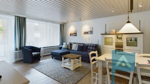 A modern living room with a sofa, a dining table with chairs, a radiator, and a window with curtains. - In 2nd row to the beach - Gmelinstraße 8 (Wyk auf Föhr)