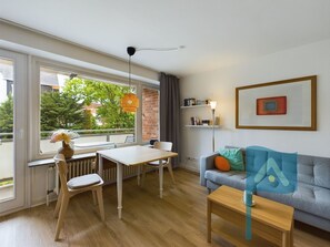 Una sala de estar moderna con comedor, ventanas amplias, un radiador, un sofá, una mesa de centro y una estantería.