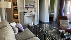 Una sala de estar moderna con una mesa de centro de vidrio, un sofá con cojines, una chimenea y vistas al dormitorio contiguo.