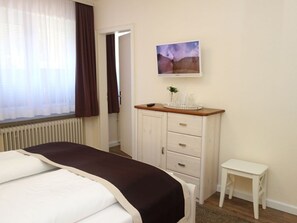 A bedroom with a bed, a dresser, a small table, and a TV on the wall.