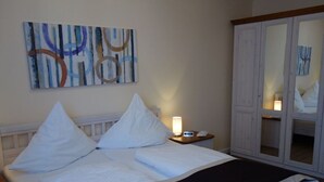 A neatly made bed with white linens and a black blanket, a bedside table with a lamp, and a wardrobe with a mirror.