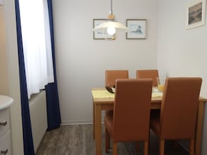 Un coin repas comprenant une table et quatre chaises, un luminaire suspendu et des tableaux encadrés accrochés au mur.