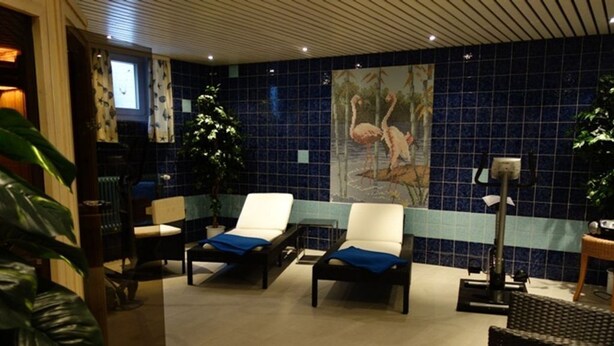 A room with two lounge chairs, a large painting of flamingos, and a tiled wall.