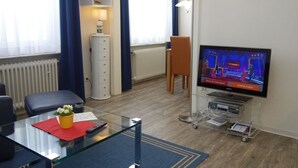 A modern living room with a glass coffee table, a television, a bookshelf, and a radiator.