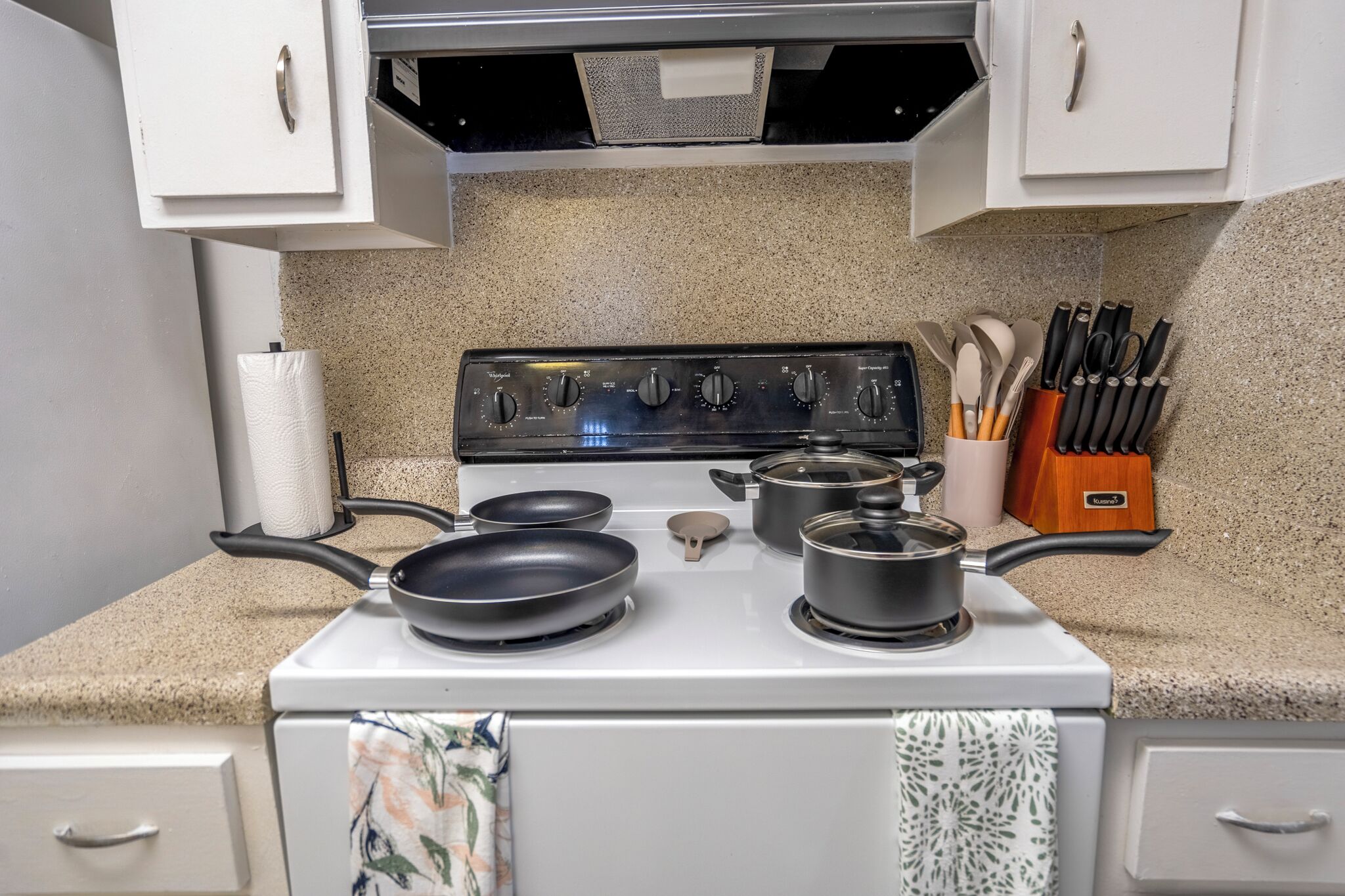 A kitchen with a white stove, four burners, a range hood, and a knife block.
