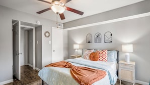 A bedroom with a bed, nightstands, a ceiling fan, and wall decorations.