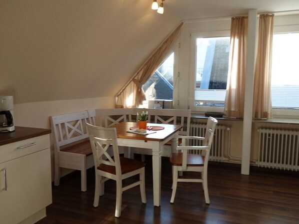 A dining area with a table and chairs, a radiator, and a window with curtains.